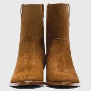 May include: A pair of brown suede ankle boots. The boots have a rounded toe, a low heel, and a pull tab at the top of the shaft. The boots are a warm brown color and appear to be made of suede.