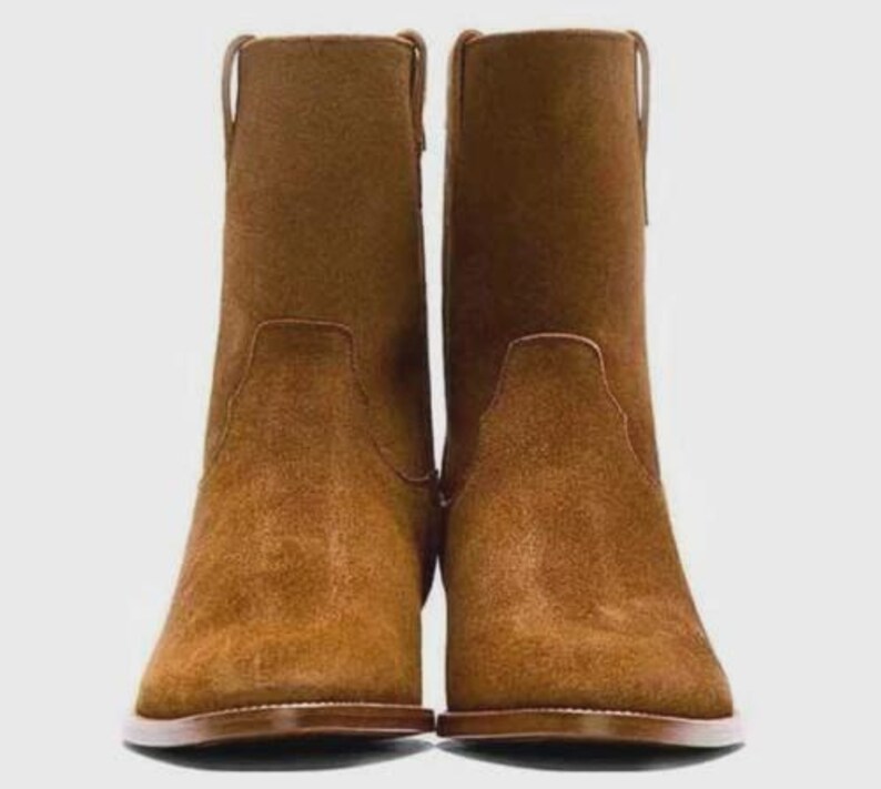 May include: A pair of brown suede ankle boots. The boots have a rounded toe, a low heel, and a pull tab at the top of the shaft. The boots are a warm brown color and appear to be made of suede.