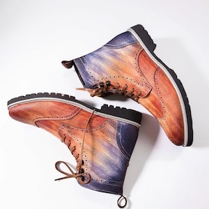 May include: A pair of leather boots with a unique painted design. The boots feature a gradient of colors, including orange, purple, and brown, with brown laces and black soles. The boots have a classic brogue style with decorative perforations.