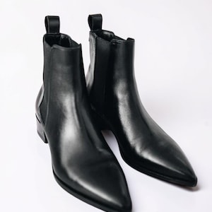 Peut inclure: Une paire de bottines Chelsea en cuir noir avec des bouts pointus. Les bottines ont des panneaux latéraux élastiques et des tirettes à l'arrière. Les petits talons offrent un look élégant et moderne. Ces bottines conviennent à diverses occasions.