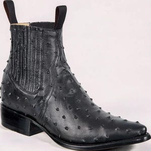 May include: Black leather ankle boot with a pointed toe and a low heel. The boot features a textured surface with small, raised bumps and pull tabs at the top. The design includes elastic side panels for easy wear.