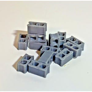 May include: A collection of small, gray concrete blocks. Each block has three rectangular holes. The blocks are scattered across a white surface, with some blocks stacked on top of each other. The blocks are likely miniature models or toys.