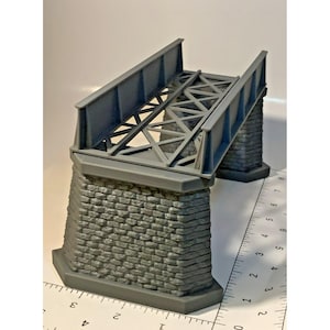 May include: A gray model bridge with a brick-like base and a metal truss design. The bridge has a sloped design and is likely for a model train set or diorama. The bridge is approximately 4 inches long.