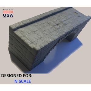 Puede incluir: Un puente de piedra gris en miniatura con una superficie texturizada, diseñado para maquetas a escala N. La imagen incluye el texto "MADE IN THE USA" y "DESIGNED FOR: N SCALE".