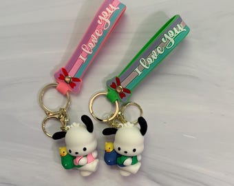 May include: Two silicone keychains featuring a white cartoon dog character with black ears, each carrying a small yellow duck in a pouch. The straps are pink and green with the text I love you and a red bow detail, attached to gold metal rings.