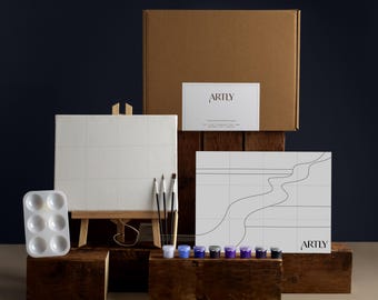 May include: A paint-by-numbers art kit with a canvas, paints, brushes, and a palette. The kit includes a small wooden easel, a paint palette, and a cardboard box. The canvas is white with a grid pattern. The text "ARTLY" is visible on the box and the canvas.