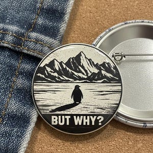 May include: A round button with a black and white illustration of a penguin standing on ice in front of mountains. The text "BUT WHY?" is printed below the penguin.