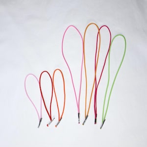 May include: A collection of six elastic cord loops in various bright colors including light pink, red, orange, magenta, and lime green. Each cord is folded into a loop and secured at the base with a small, cylindrical silver-toned metal crimp.