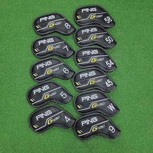 Puede incluir: Un conjunto de fundas para palos de golf PING G430 negras, cada una etiquetada con un número o letra. Las fundas tienen un diseño amarillo y blanco, y están dispuestas sobre una superficie verde.
