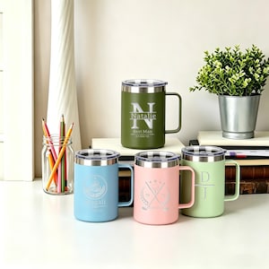 Pode incluir: Quatro canecas de viagem isoladas em verde, azul, rosa e verde claro, cada uma com tampa e alça prateadas. As canecas são personalizadas com nomes, iniciais e datas. Uma pequena planta e lápis estão no fundo.