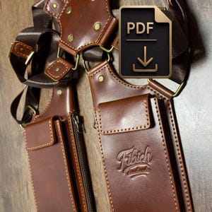 Könnte beinhalten: Braunes Leder-Schulterholster mit zwei Taschen, genähten Kanten und messingfarbener Hardware. Das Holster hat verstellbare Riemen und der Text "Fibich handmade" ist auf einer Tasche geprägt.