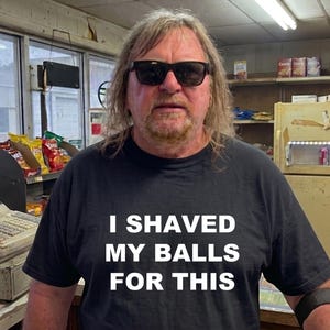 May include: A person wearing a black t-shirt with the text "I shaved my balls for this." The person is wearing sunglasses and standing in a convenience store setting.