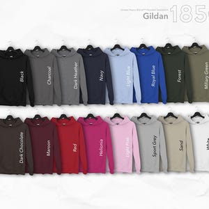May include: A collection of Gildan 18500 hooded sweatshirts in various colors, including black, charcoal, navy, light blue, and forest green. Each sweatshirt is displayed on a hanger, showcasing the different hues available.