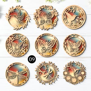 May include: A collection of nine circular wooden ornaments featuring intricate laser-cut designs of butterflies, hummingbirds, and dragonflies. Each piece has a colorful, gradient-style background insert and is labeled with the number 09.