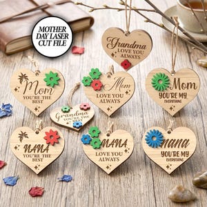 May include: Wooden heart-shaped ornaments with floral accents and text for Mother's Day. The ornaments say "Mom," "Grandma," and "Nana," with phrases like "Love You Always" and "You're the Best." The image also includes the text "Mother Day Laser Cut File."