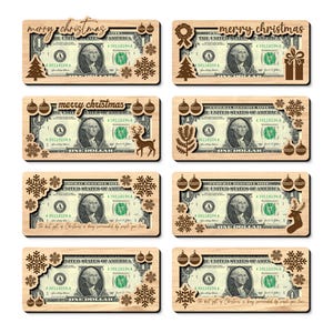 May include: Eight rectangular light-coloured wooden money holders, each framing a one-dollar bill. The frames feature laser-cut designs including snowflakes, Christmas trees, ornaments, reindeer, and the text Merry Christmas or The best gift of Christmas.