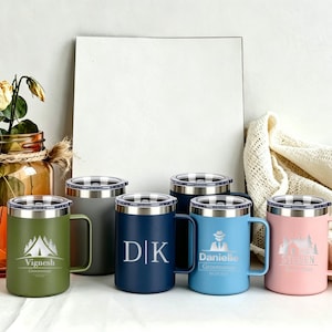 May include: A collection of insulated travel mugs in various colors, including green, navy, blue, and pink. Each mug features a silver lid and handle, with personalized text and graphics. A decorative jar with flowers is in the background.