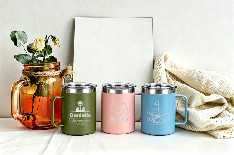 May include: Three insulated travel mugs in olive green, pink, and light blue. Each mug has a silver lid and handle. The olive green mug has a graphic of a person in a hat and the name "Danielle". The pink mug has a whale graphic. The blue mug has a golf graphic.