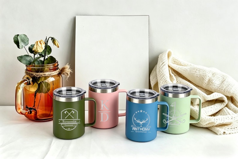 May include: Four insulated travel mugs in green, pink, blue, and light green, each with a silver lid and handle. The green mug has an axe design and the name "Soumia". The pink mug has the initials "KD". The blue mug has a deer design and the name "Anthony". The light green mug has a golf club design.