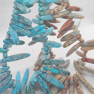 May include: A necklace featuring elongated, polished beads in shades of turquoise, brown, and beige. The beads are strung together, creating a layered effect. The necklace is displayed against a white background.