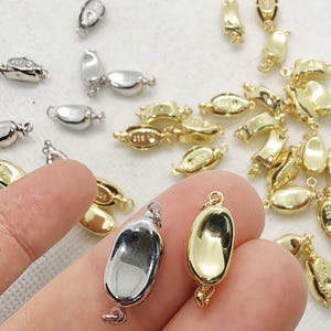 May include: An assortment of silver and gold-coloured jewellery clasps. The clasps are oval-shaped with a loop at the top and a small clasp at the bottom. Some clasps are silver, others are gold.