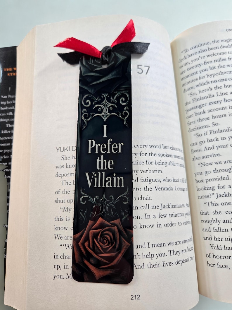 Może przedstawiać: Czarna zakładka do książki z napisem "I Prefer the Villain" i ilustracją czerwonej r&oacute;ży. Zakładka ma przymocowaną czarną i czerwoną wstążkę i jest umieszczona w otwartej książce.