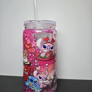 K&ouml;nnte beinhalten: Ein klarer Becher mit einem rosa-wei&szlig;en Design mit Zeichentrickfiguren, Herzen und dem Wort "Love". Der Becher enth&auml;lt einen klaren Strohhalm und einen klaren Deckel. Der Becher ist mit rosa Glitzer gef&uuml;llt.