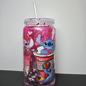 K&ouml;nnte beinhalten: Ein durchsichtiger Becher mit einer rosa und glitzernden Fl&uuml;ssigkeit im Inneren, mit Cartoon-Figuren und Herzmotiven. Der Becher hat einen durchsichtigen Deckel und einen Strohhalm. Die Figuren halten Herzen und befinden sich auf einer roten Kaffeetasse.