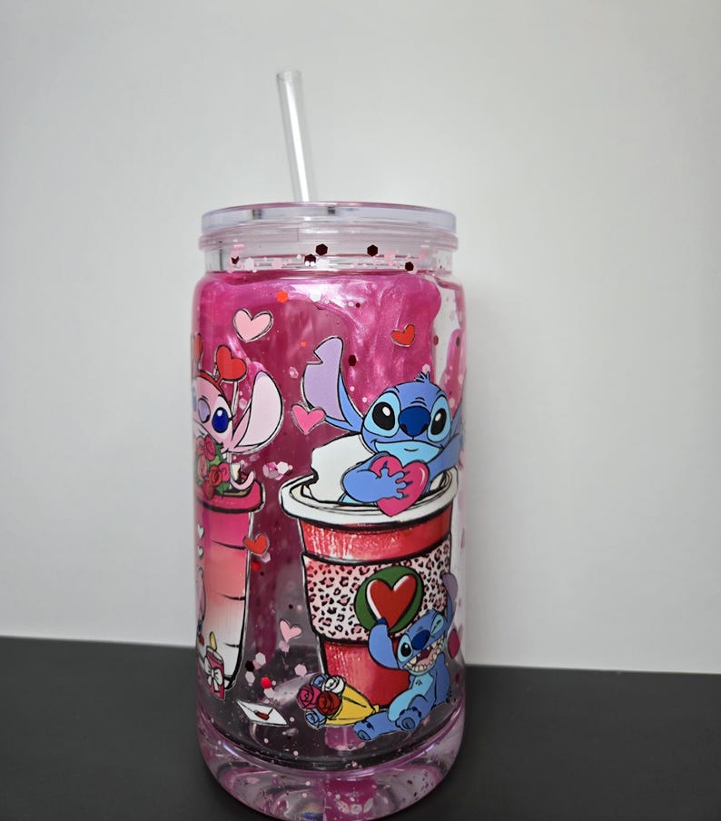 K&ouml;nnte beinhalten: Ein durchsichtiger Becher mit einer rosa und glitzernden Fl&uuml;ssigkeit im Inneren, mit Cartoon-Figuren und Herzmotiven. Der Becher hat einen durchsichtigen Deckel und einen Strohhalm. Die Figuren halten Herzen und befinden sich auf einer roten Kaffeetasse.