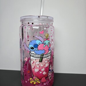 K&ouml;nnte beinhalten: Ein durchsichtiger Kunststoffbecher mit Deckel und Strohhalm, verziert mit einem Cartoon-Bild von Stitch und einem rosa Getr&auml;nk mit herzf&ouml;rmigen Eisw&uuml;rfeln. Der Becher ist mit rosa Glitzer und herzf&ouml;rmigen Konfetti gef&uuml;llt.