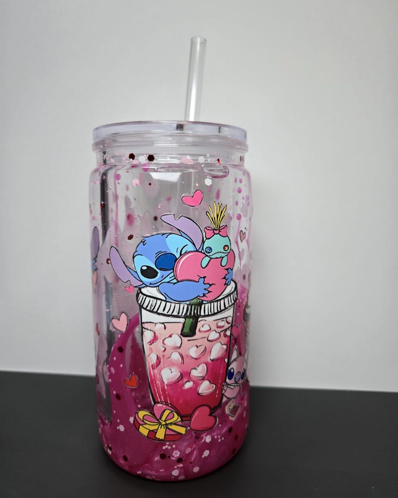 K&ouml;nnte beinhalten: Ein durchsichtiger Kunststoffbecher mit Deckel und Strohhalm, verziert mit einem Cartoon-Bild von Stitch und einem rosa Getr&auml;nk mit herzf&ouml;rmigen Eisw&uuml;rfeln. Der Becher ist mit rosa Glitzer und herzf&ouml;rmigen Konfetti gef&uuml;llt.