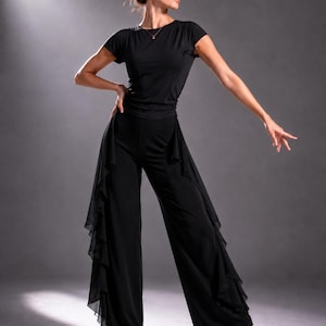 Könnte beinhalten: Ein schwarzes Tanzoutfit bestehend aus einem kurzärmeligen, eng anliegenden Oberteil und einer weiten Hose. Die Hose ist an den Außennähten mit transparenten, gerüschten Stoffbahnen versehen, die von der Taille bis zum Saum reichen.