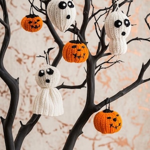 Könnte beinhalten: Eine Sammlung gehäkelter Ornamente, die an einem schwarzen dekorativen Baum hängen. Das Set enthält drei weiße Geister mit schwarz gestickten Augen und Mündern sowie drei orangefarbene Kürbisse mit schwarz gestickten Jack-o'-Lantern-Gesichtern.