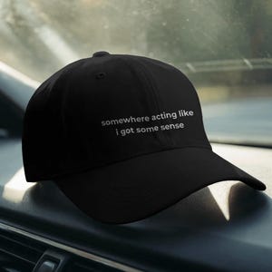 Peut inclure: Casquette de baseball noire avec une visière incurvée. Le texte blanc "somewhere acting like i got some sense" est brodé sur le devant. La casquette est faite d'une matière souple.