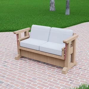 May include: A light-colored wooden outdoor loveseat with two white cushions. The armrests have a unique design with red chain accents. The loveseat is placed on a brick patio, with green grass and trees in the background.