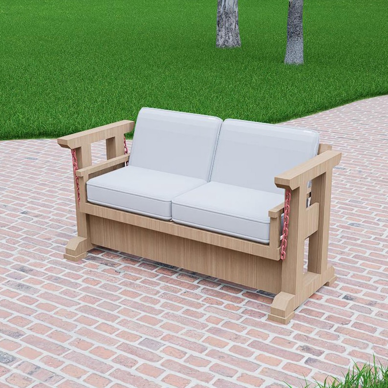 May include: A light-colored wooden outdoor loveseat with two white cushions. The armrests have a unique design with red chain accents. The loveseat is placed on a brick patio, with green grass and trees in the background.