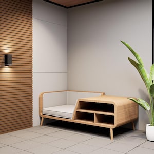 May include: Contemporary wooden bench with a white cushion and open storage. The bench is set against a light grey wall with a large potted plant. The wall has a wooden panel design with a black light fixture.