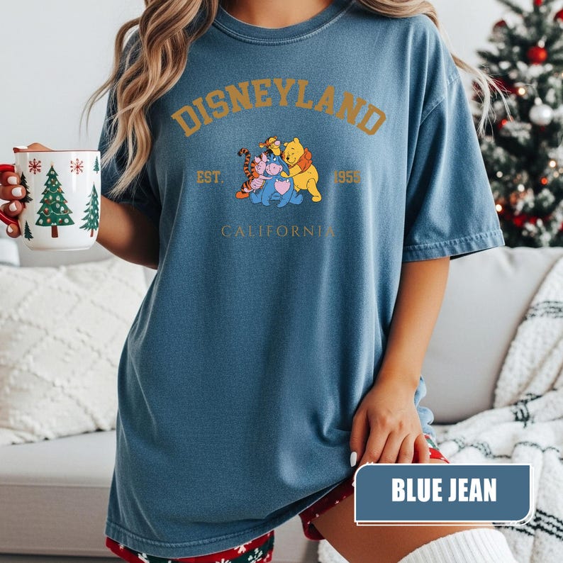 Pu&ograve; includere: T-shirt blu jeans con la scritta "DISNEYLAND" in lettere dorate. La maglietta presenta una grafica di Winnie the Pooh, Tigro, Pimpi ed Eeyore. Il testo "EST. 1955 CALIFORNIA" &egrave; stampato anche sulla maglietta.