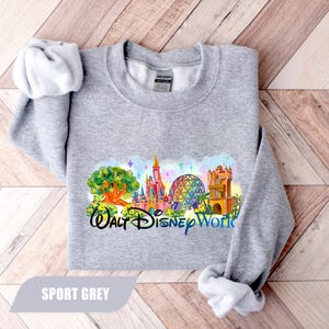 May include: Sport grey sweatshirt featuring a colorful graphic of Walt Disney World landmarks. The design includes a castle, a geodesic sphere, and other park icons. The text "Walt Disney World" is printed below the graphic in black and blue.