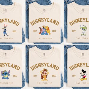 Pu&ograve; includere: T-shirt color crema con la scritta "DISNEYLAND" in oro ad arco. Ogni maglietta presenta una grafica diversa di un personaggio Disney, tra cui Judy Hopps, Winnie the Pooh, Buzz Lightyear, Stitch, Belle e Topolino. Il testo "EST. 1955 CALIFORNIA" &egrave; anch'esso stampato.