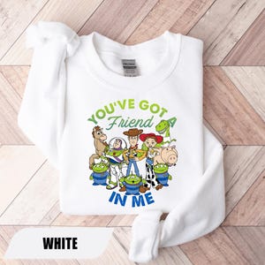 May include: White sweatshirt featuring a graphic of characters from the movie Toy Story. The text "YOU'VE GOT A FRIEND IN ME" is printed in green and blue. The sweatshirt is made of a soft material.