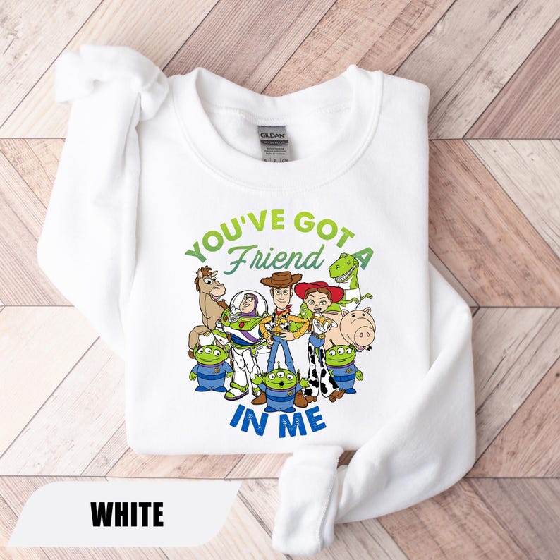 May include: White sweatshirt featuring a graphic of characters from the movie Toy Story. The text "YOU'VE GOT A FRIEND IN ME" is printed in green and blue. The sweatshirt is made of a soft material.