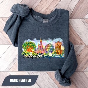 May include: Dark heather gray sweatshirt featuring a colorful watercolor design of Walt Disney World landmarks. The design includes the Tree of Life, Cinderella Castle, Spaceship Earth, and Tower of Terror. The text "Walt Disney World" is also included.