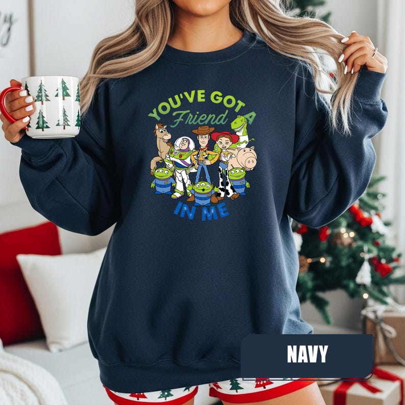 May include: Navy blue sweatshirt featuring a colorful graphic of characters from the animated film "Toy Story." The design includes the text "You've Got a Friend in Me." The sweatshirt is a crew neck style.