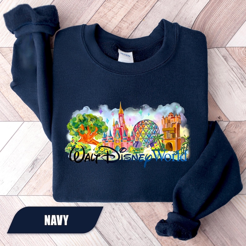 May include: Navy blue sweatshirt featuring a colorful graphic of the Walt Disney World logo and various park landmarks. The design includes a castle, Spaceship Earth, and other iconic elements. The word "NAVY" is displayed on the bottom left.