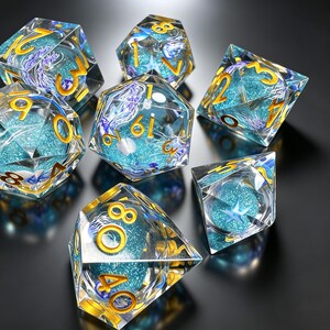 May include: A set of polyhedral dice made of clear resin, each containing a blue glitter core, purple jellyfish-like inclusions, and a small white starfish. The numbers on the faces of the dice are engraved and filled with a metallic gold pigment.