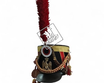 May include: A black military bicorne hat with a red plume. The hat features gold trim, a red and black stripe, and a gold emblem. Tassels and a braided rope adorn the sides. The hat has a small brim.