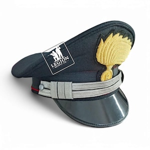 May include: A dark navy military hat with a glossy black peak, silver band, and gold embroidered emblem. The hat has a white square with the text "LEGION - SUPPLY CO." and a graphic of two soldiers.