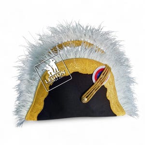 Puede incluir: Un sombrero bicornio negro con ribetes dorados y plumas blancas. El sombrero presenta un cordón dorado y una roseta roja, blanca y azul. El sombrero tiene una etiqueta que dice "LEGION SUPPLY CO."
