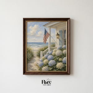 May include: Framed art print depicting a coastal scene with a white porch, American flag, and blue and white hydrangeas. The artwork features a path leading to the beach under a blue sky with clouds. The frame is dark brown.